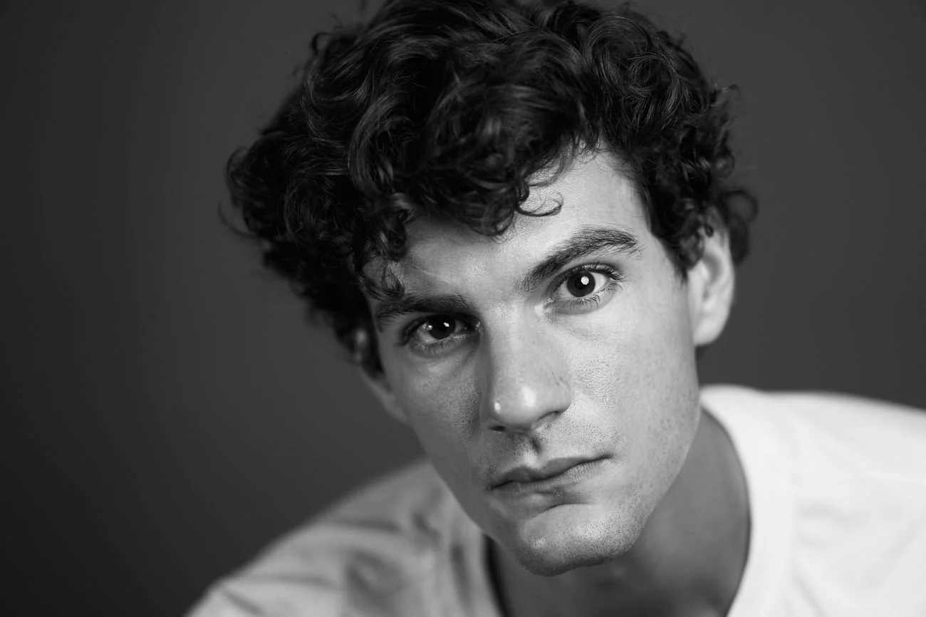 Black-and-white actor headshot with tilted head and curly hair