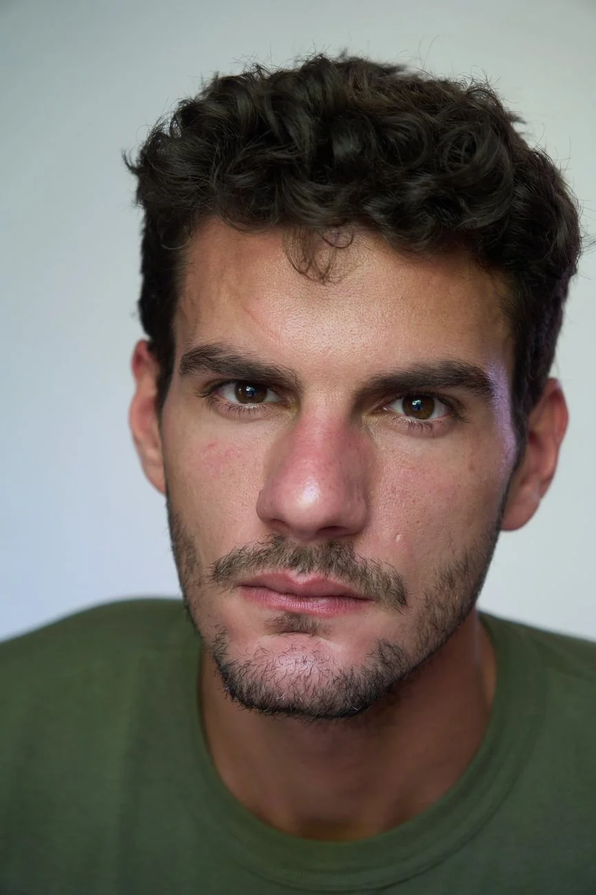 Actor headshot of a man with dark curly hair in a green t-shirt, shot in natural light